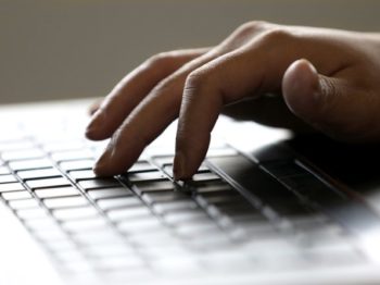 A photo of a hand typing at a laptop keyboard.